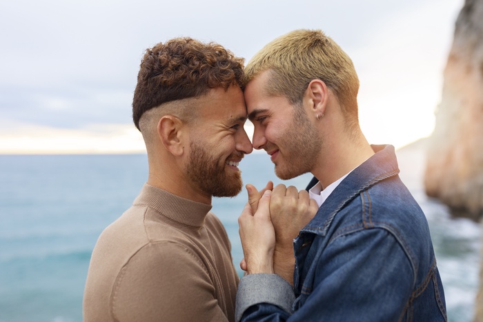 Two men share a gentle, loving moment by the sea.