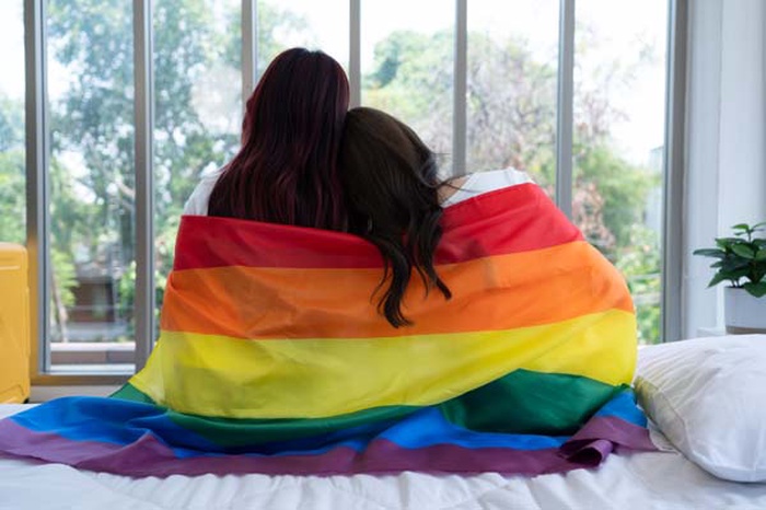  The LGBT couple sat on the bed covered in rainbow flags peering out the window to observe  the nature in the hotel room