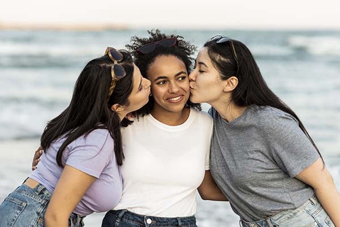  Three female friends kissing each other on the beach